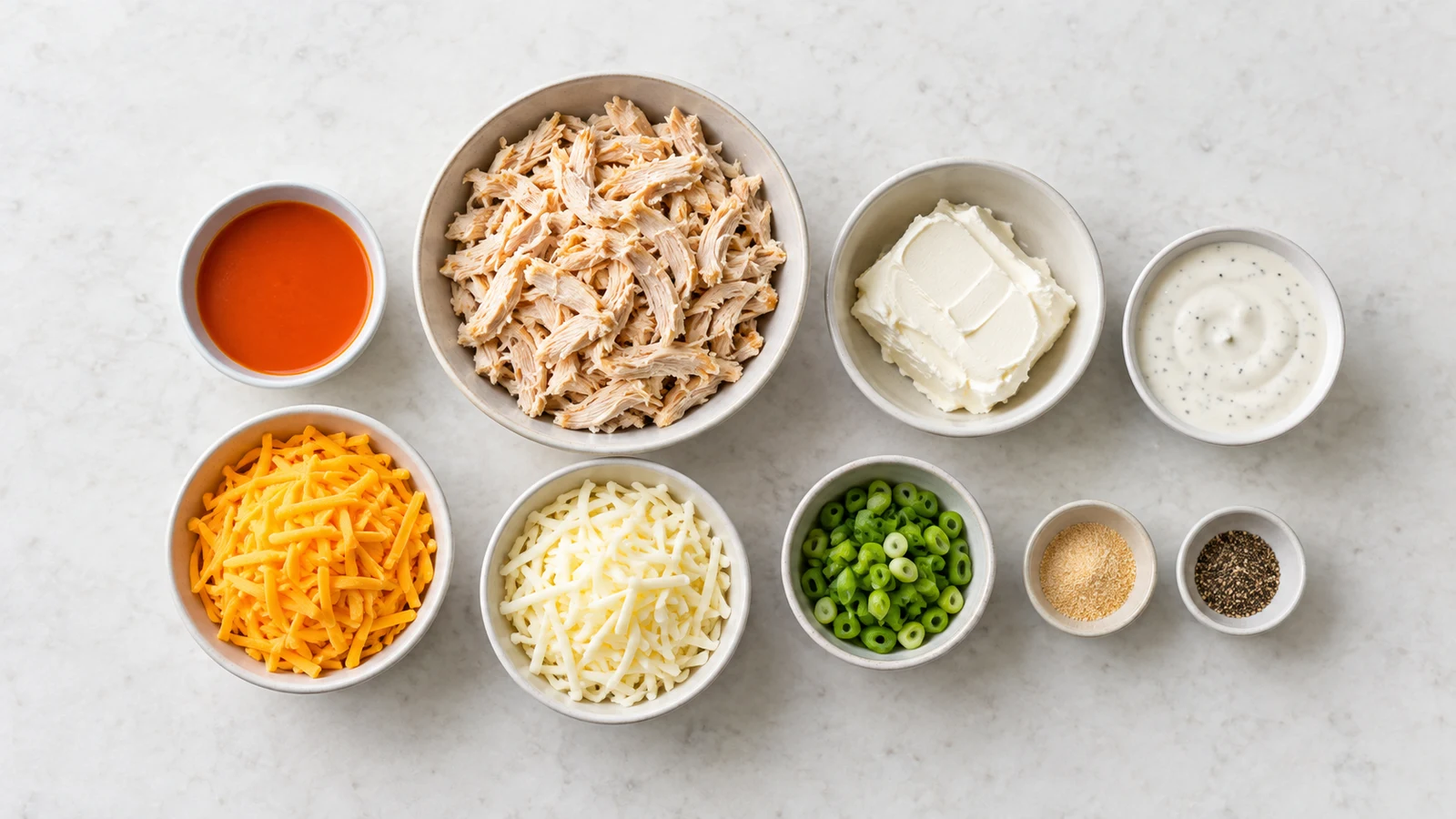 Buffalo chicken dip recipe: ingredients for buffalo chicken dip arranged in bowls, including chicken, cheeses, Buffalo sauce, and ranch.