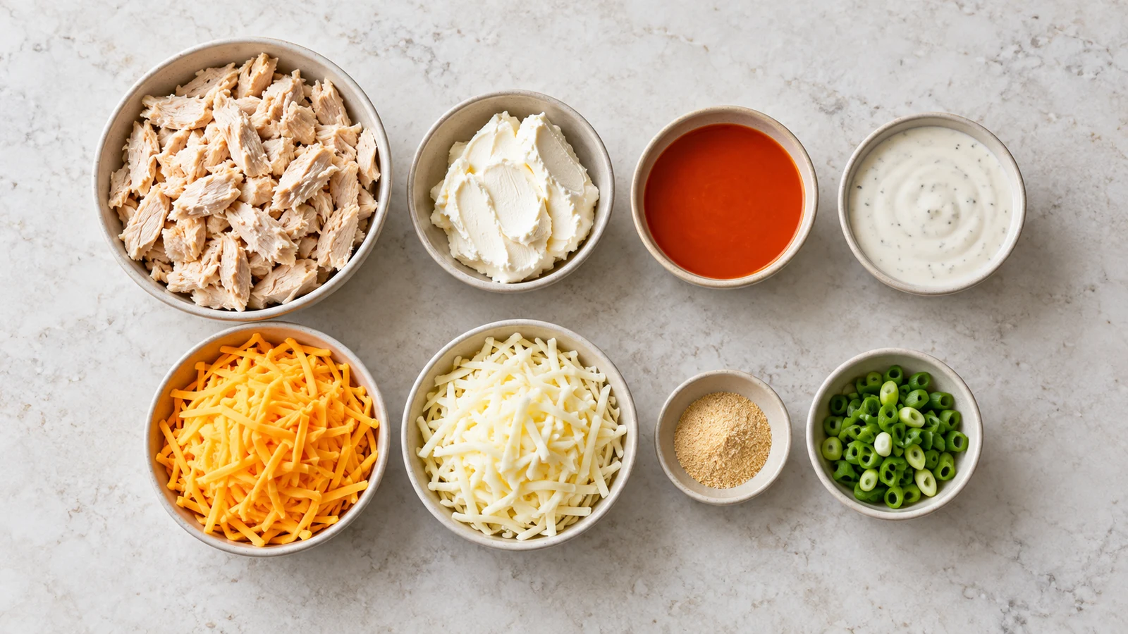 Ingredients for buffalo chicken dip with canned chicken arranged in bowls on a light surface.