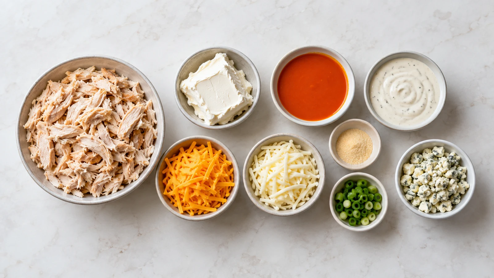 Buffalo dip ingredients arranged in bowls, including chicken, cheeses, Buffalo sauce, ranch, and green onions.