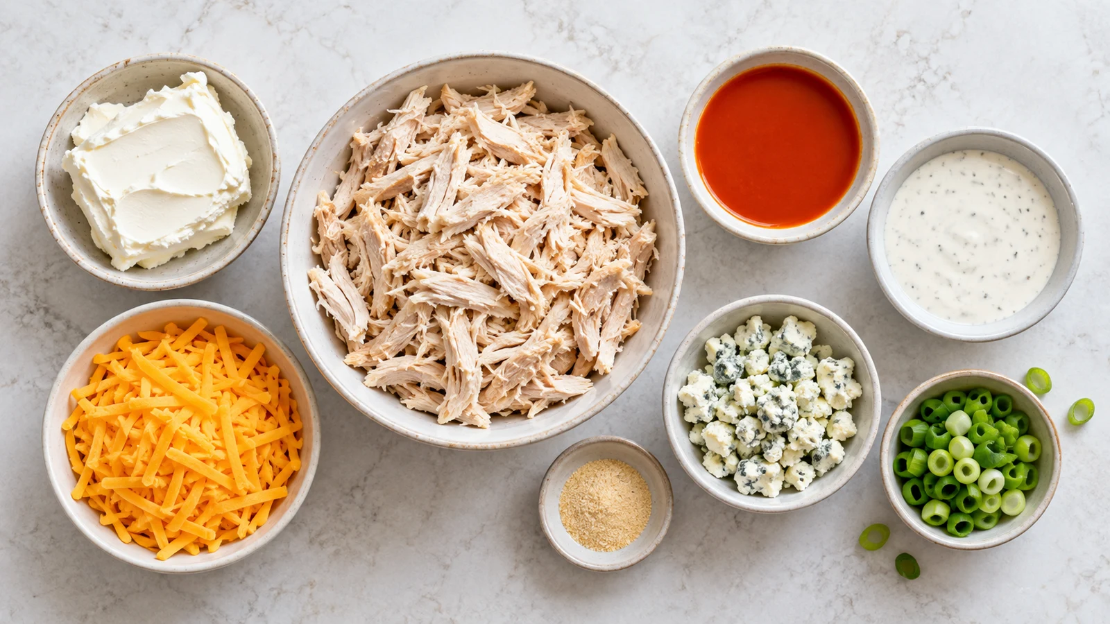 Ingredients for crock pot buffalo chicken dip arranged in bowls on a bright, clean surface.