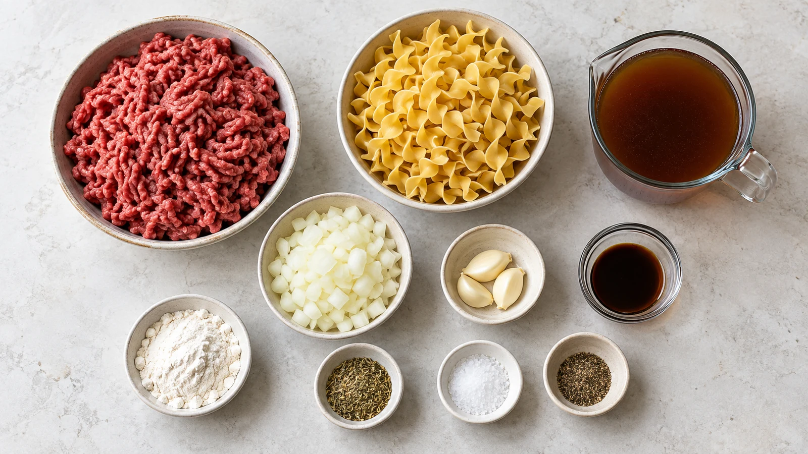 Ground beef and noodles recipe: ingredients for ground beef and noodles arranged in bowls on a light surface.